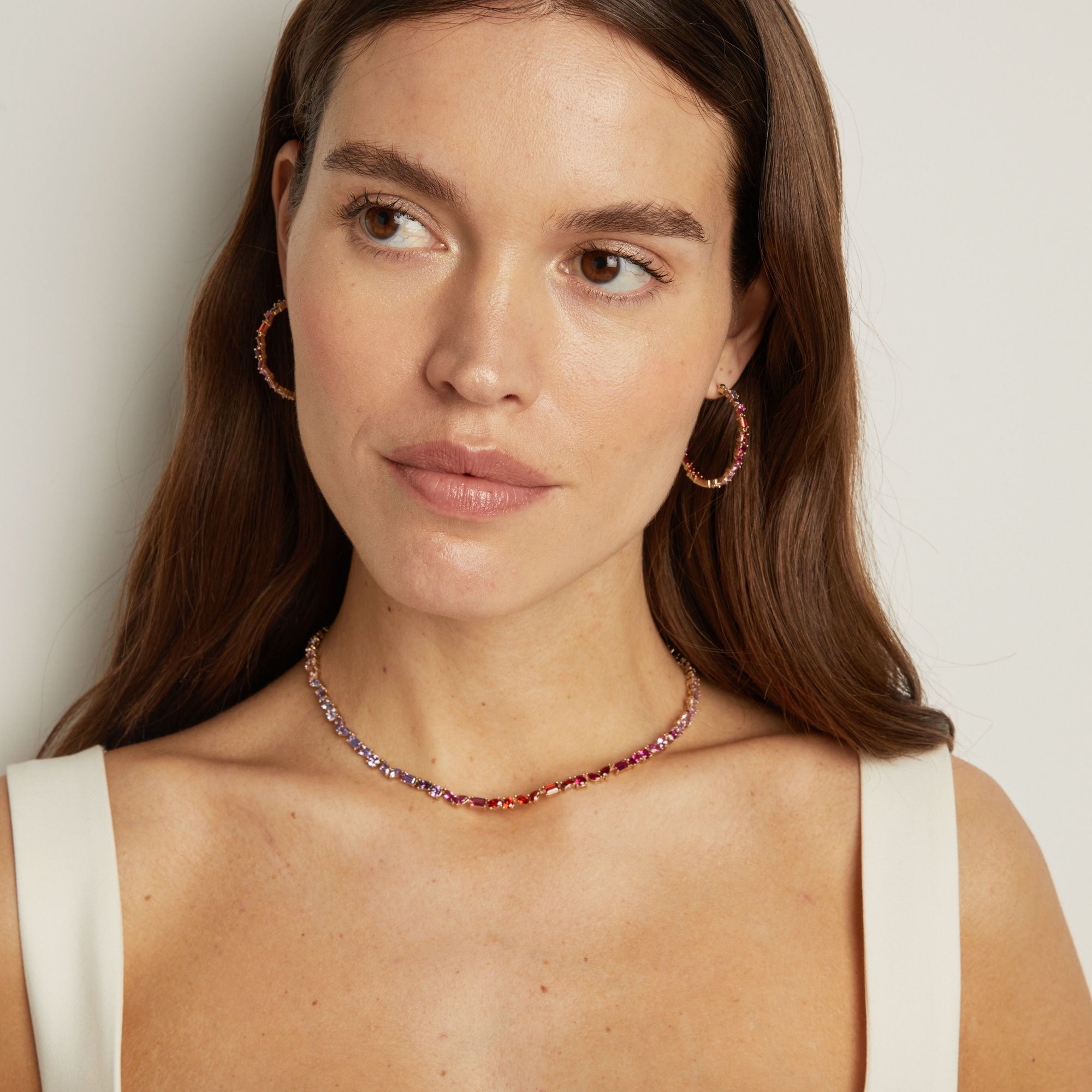 Model. Woman wearing a necklace and hoop earrings against a neutral background