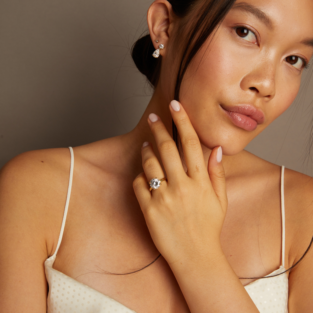 Model. Woman wearing a diamond ring and earrings against a neutral background