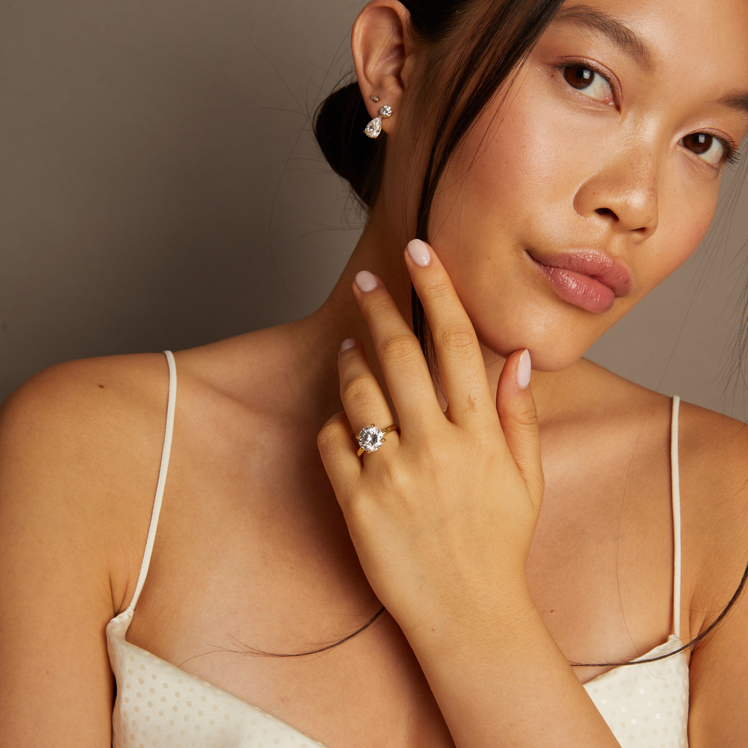 Model. Woman wearing a diamond ring and earrings against a neutral background