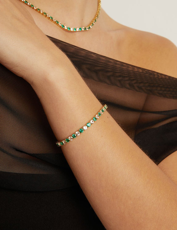 Close-up of a person wearing a gold bracelet with green stones on a neutral background