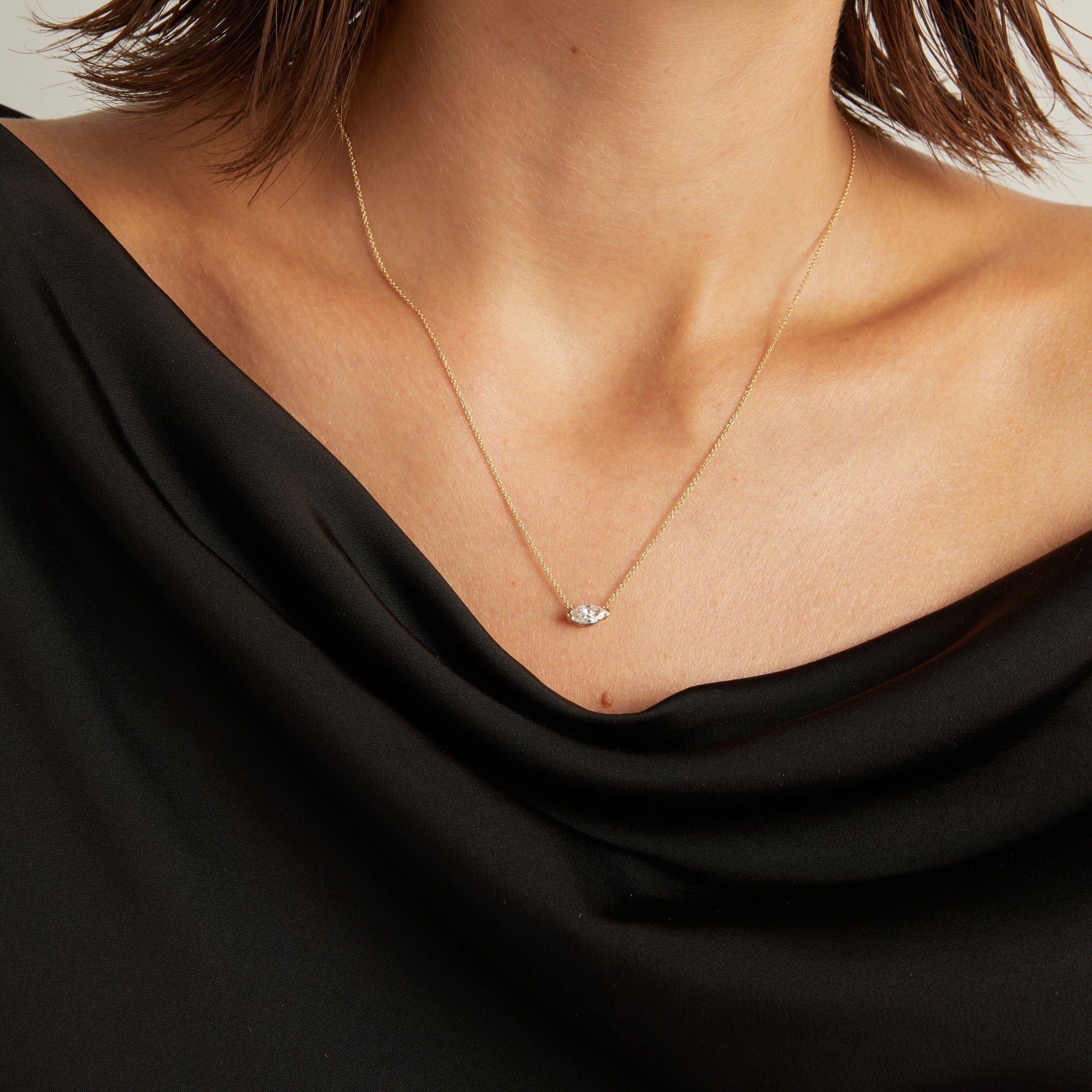 Model. Close up of woman wearing a black top with a marquise diamond solitaire necklaces on a beige background.