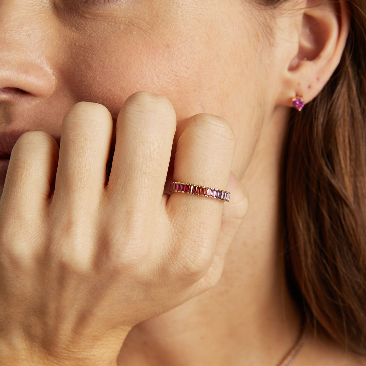 Model. Close-up of a woman wearing a pink ring and earring, with her hand near her face.