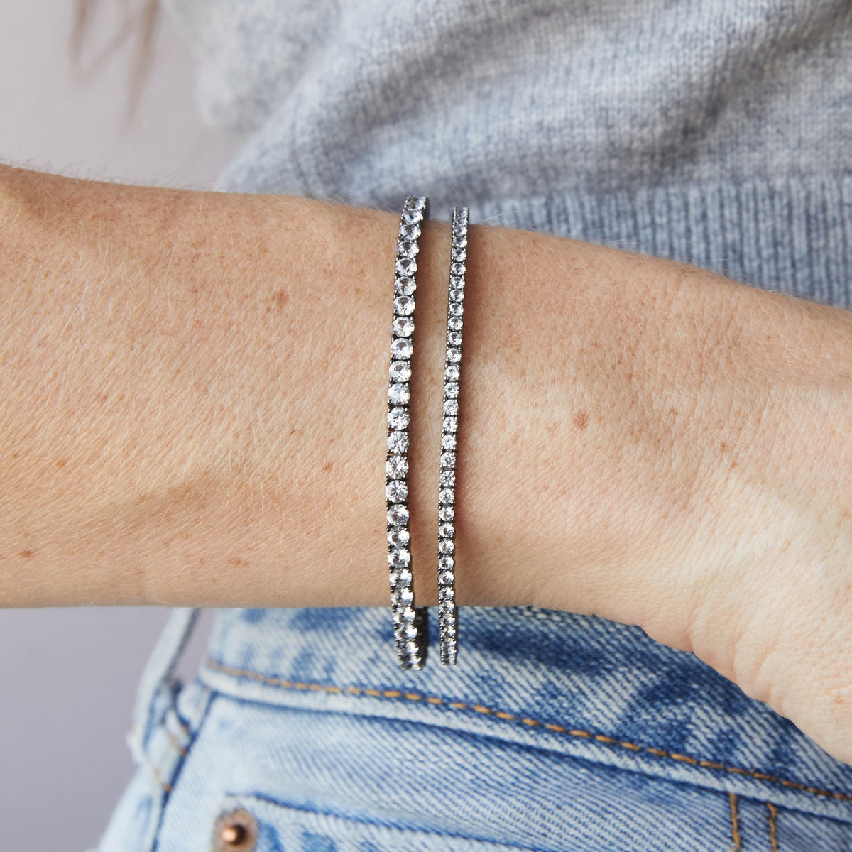 Model. Close up of woman's wrist wearing two black rhodium tennis bracelets