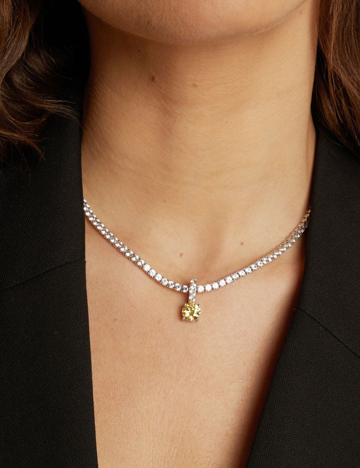 Tennis necklace with a round gemstone pendant worn by a person against a neutral background.