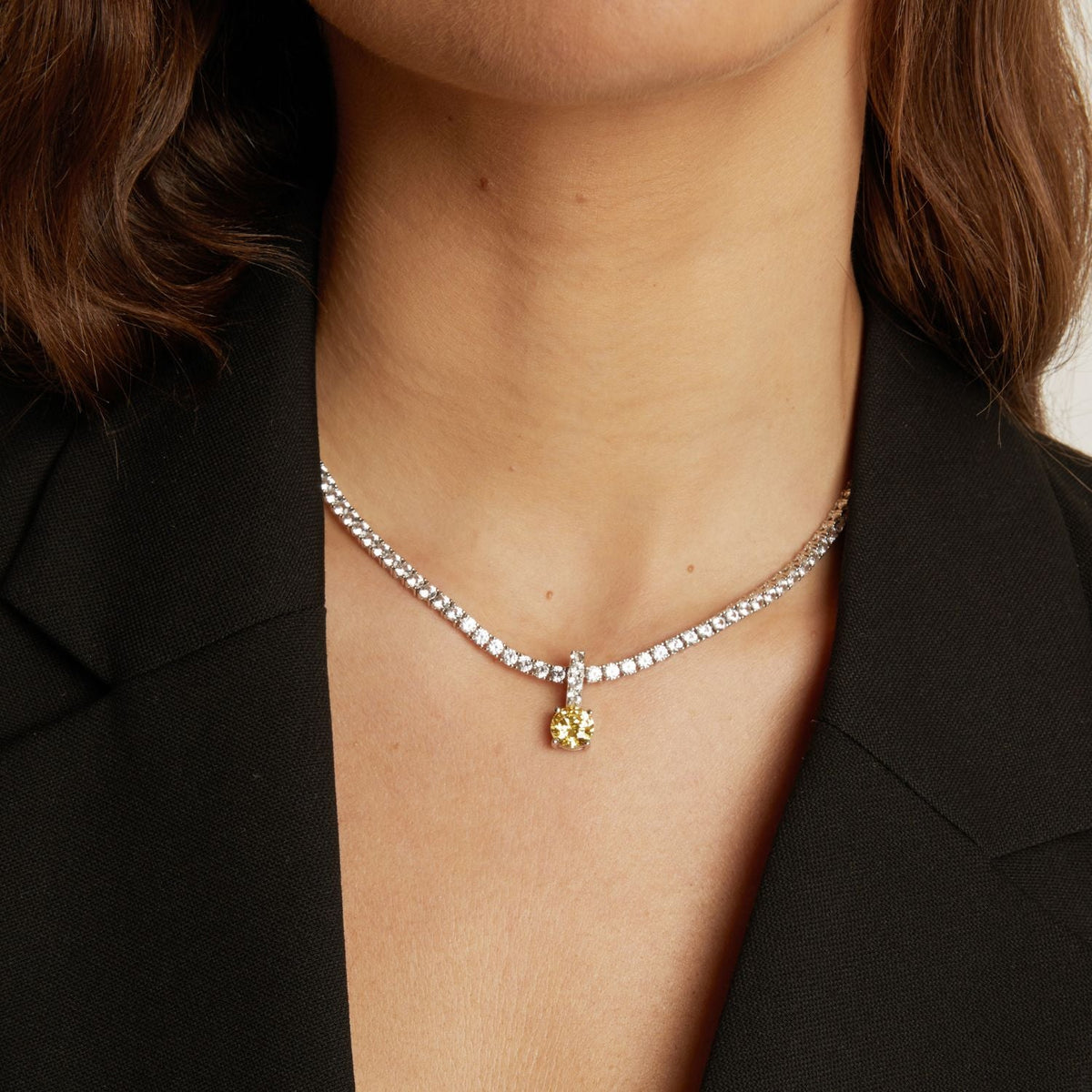 Tennis necklace with a round gemstone pendant worn by a person against a neutral background.