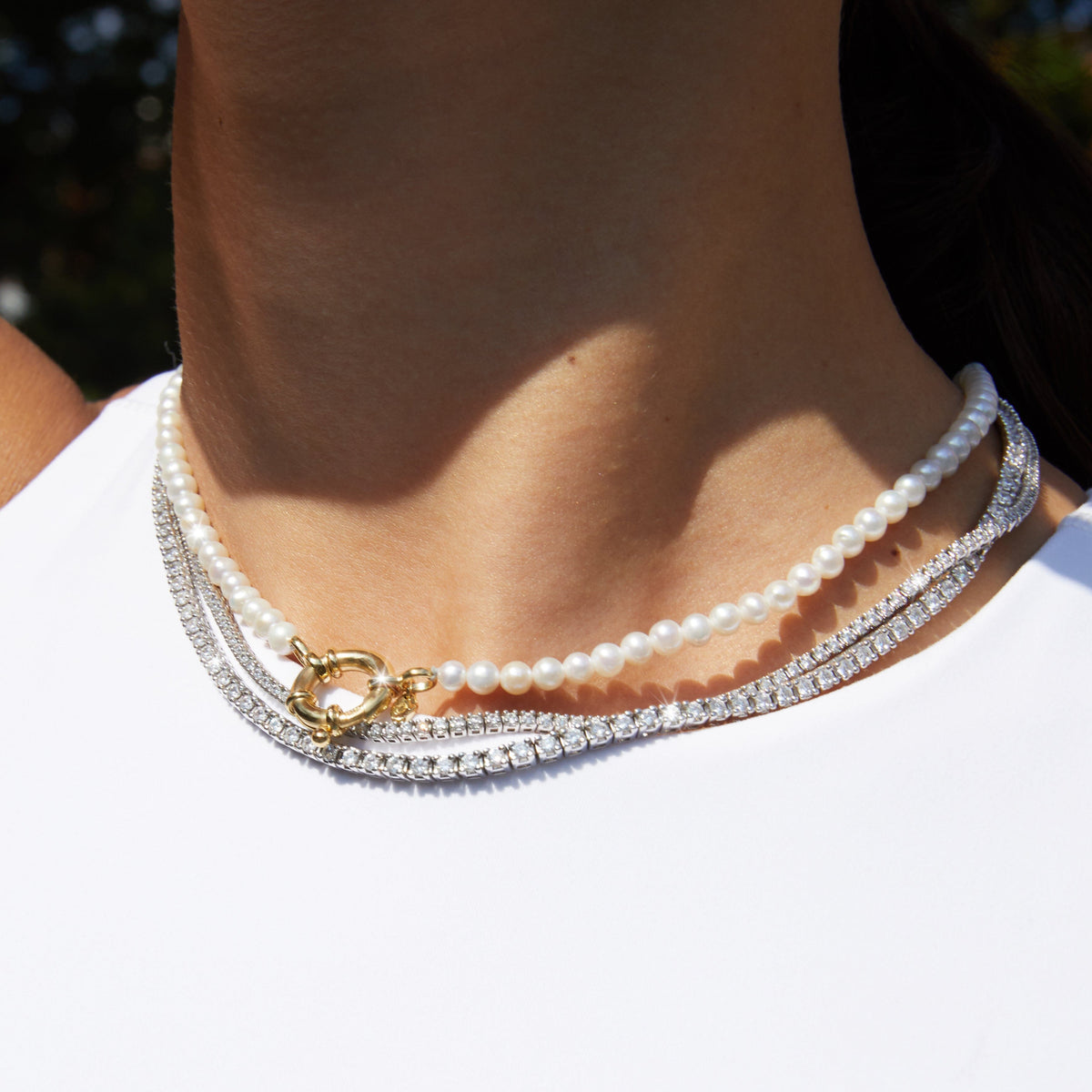 Lifestyle Model Woman wearing a pearl necklace with a gold toggle clasp layered with a diamond tennis necklace
