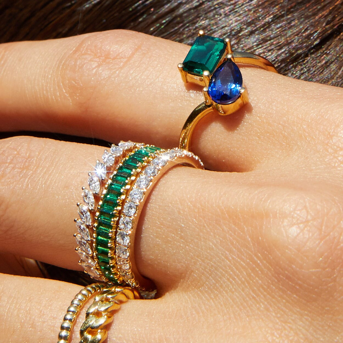 Lifestyle Model Close-up of a woman resting her hand near her hair, wearing multiple gold rings featuring green and blue stones