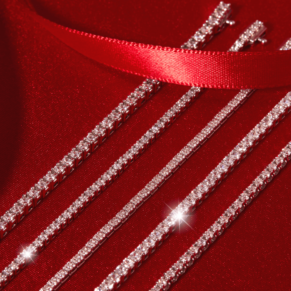 Flatlay Model Four diamond tennis chains arranged diagonally across a dark red background, accented by a red satin ribbon.