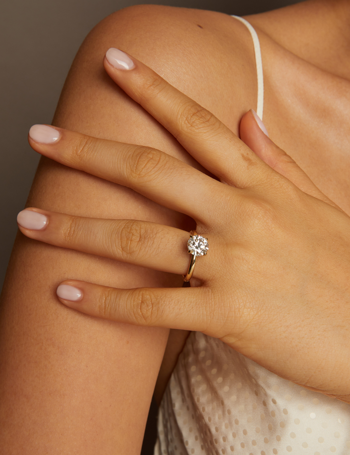 Hand wearing a gold ring with a diamond, resting on a shoulder against a neutral background