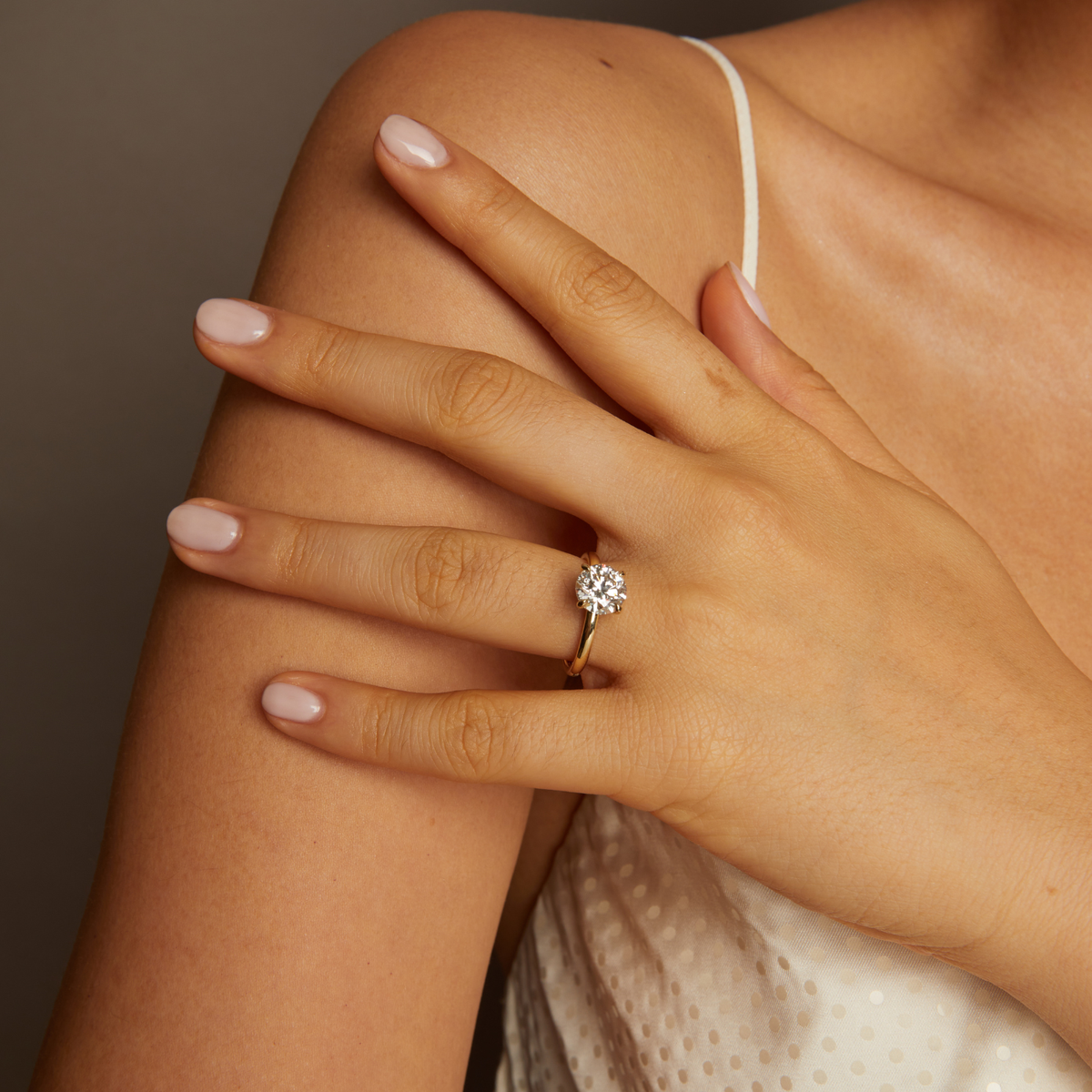 Hand wearing a gold ring with a diamond, resting on a shoulder against a neutral background