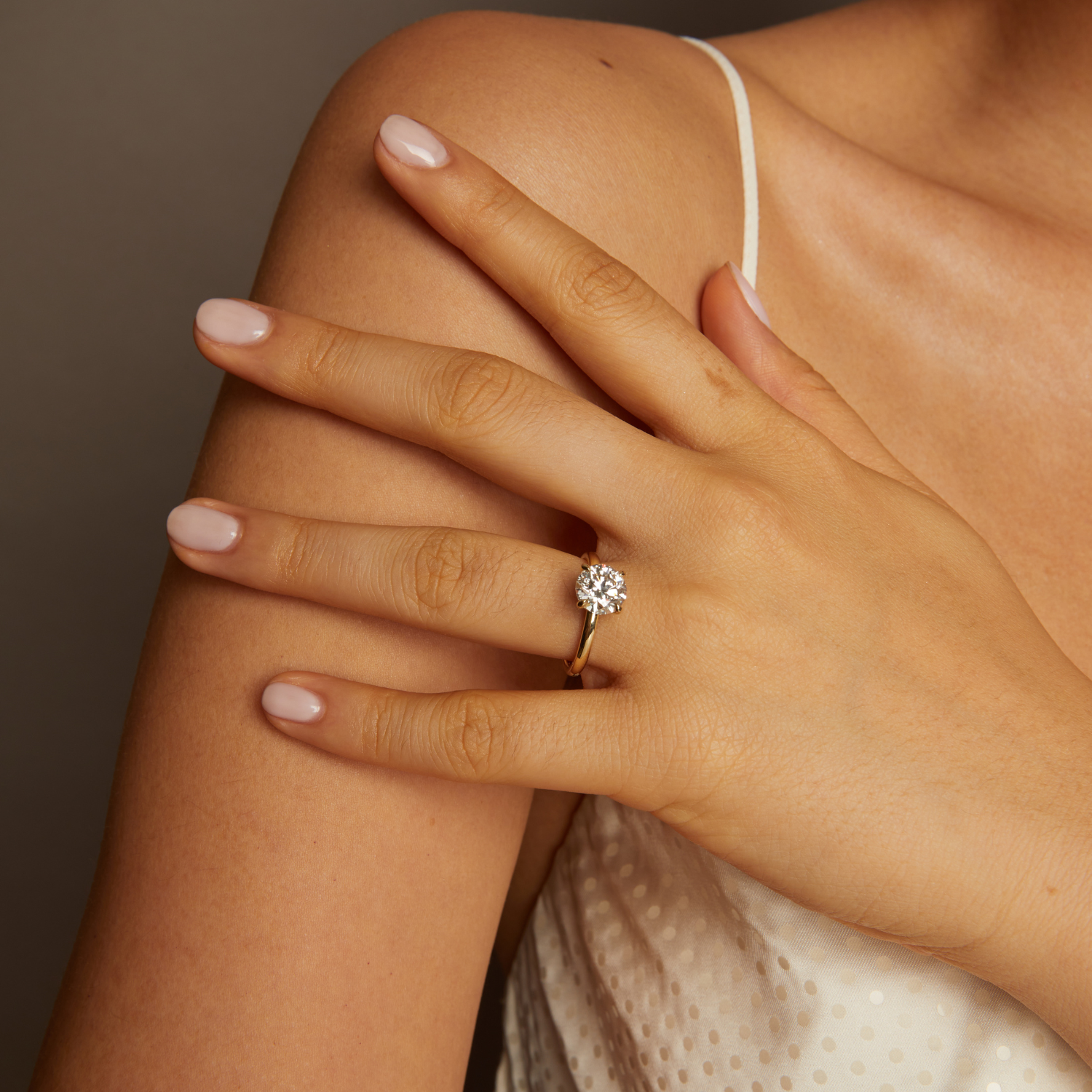 Hand wearing a gold ring with a diamond, resting on a shoulder against a neutral background