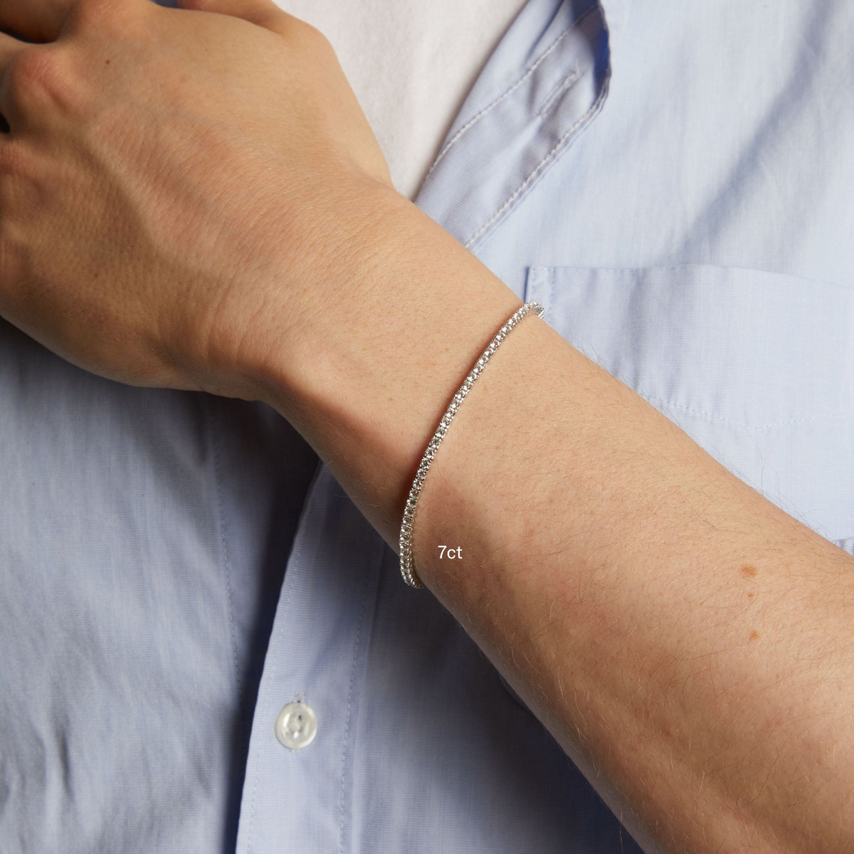 Model. A close-up of a man's wrist wearing a delicate tennis bracelet, shown against a light blue button-down shirt.