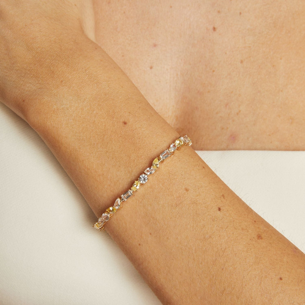 Gold bracelet with embedded stones on a person's wrist against a neutral background