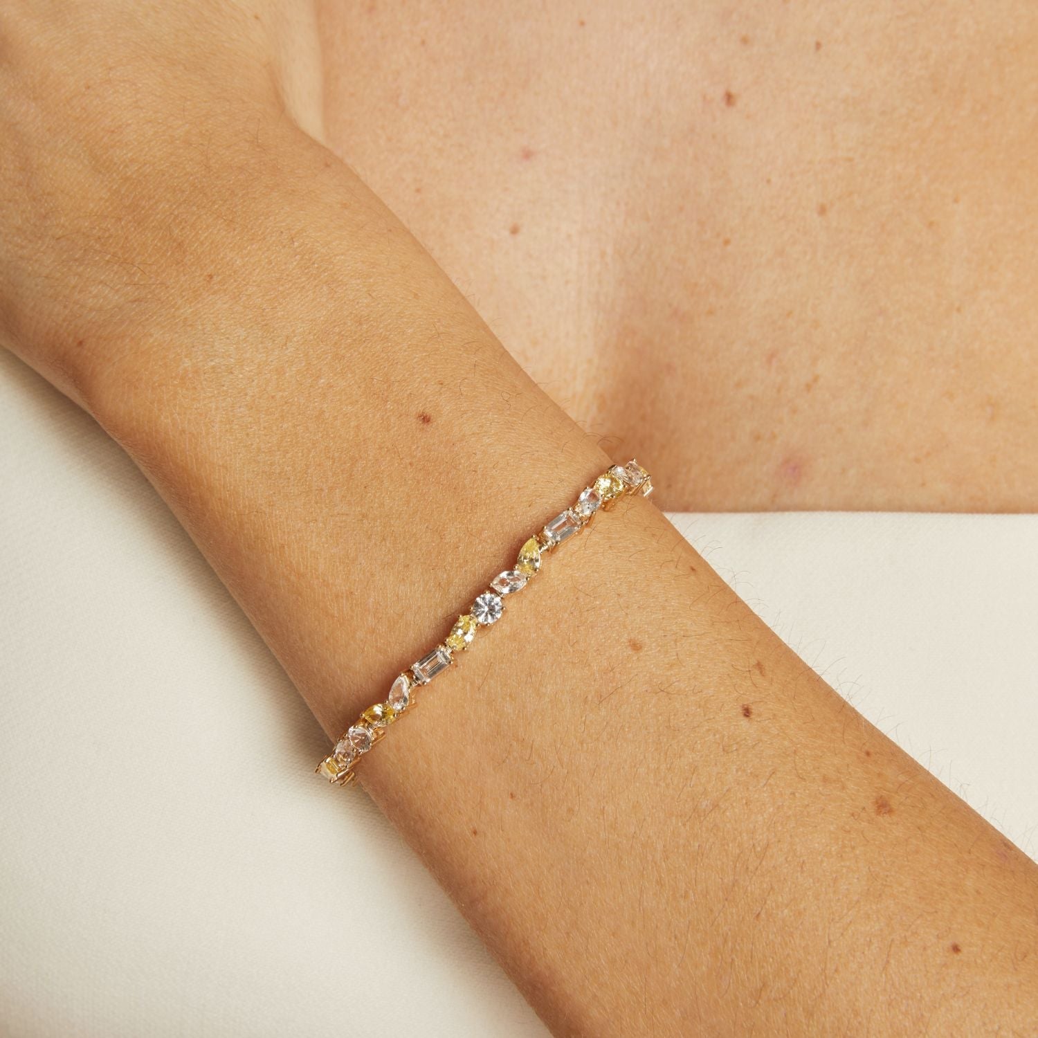Gold bracelet with embedded stones on a person's wrist against a neutral background