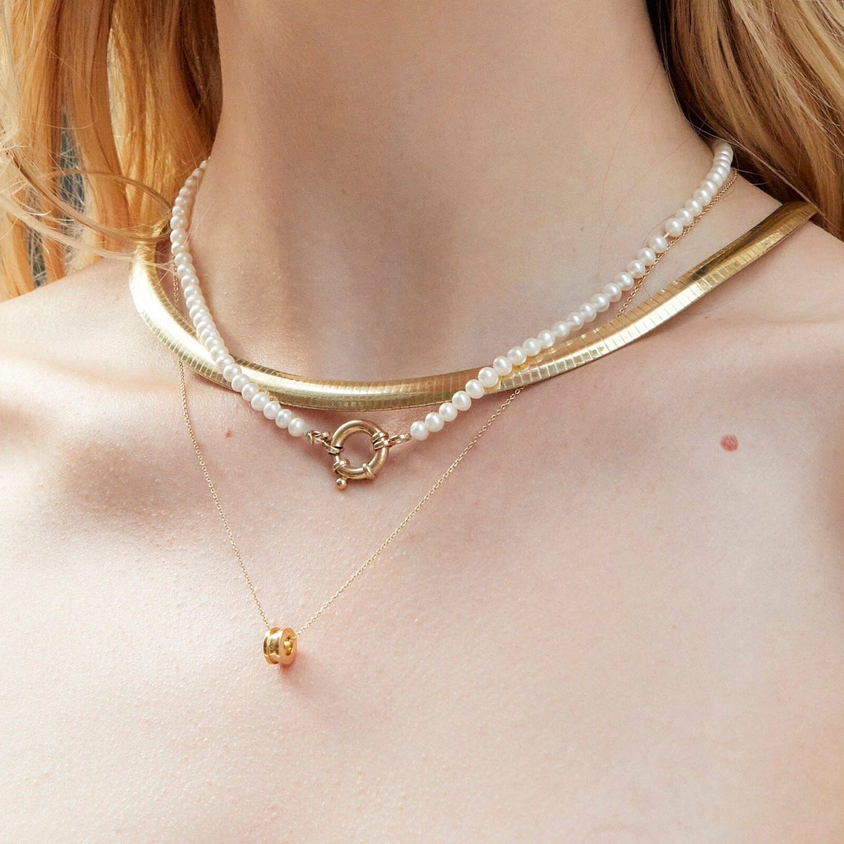Lifestyle Model "Close-up of a woman wearing layered necklaces, including a pearl choker, a thick gold snake chain, and a delicate gold chain with a small column pendant.