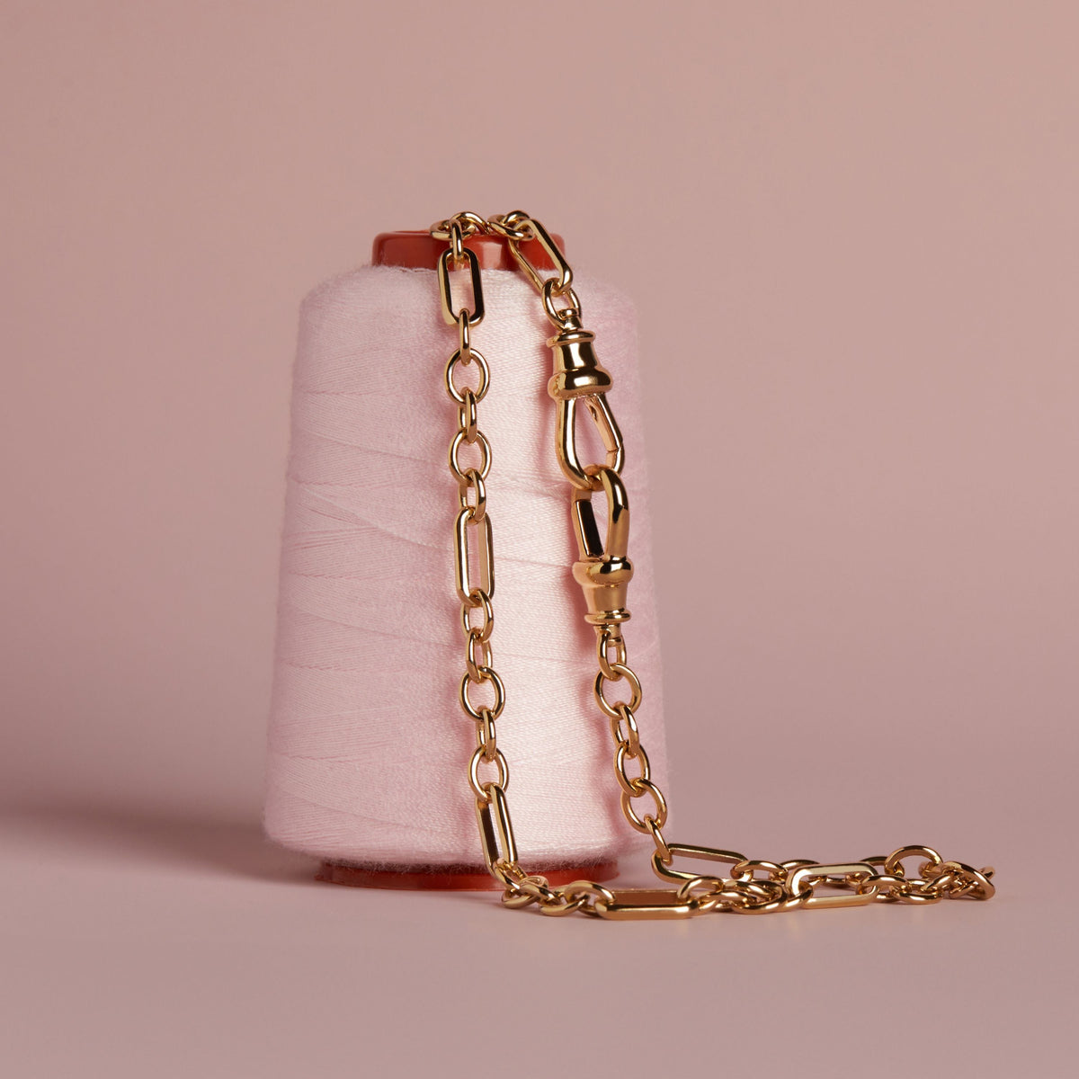 Model. Close up of gold chain necklace on thread spool. 
