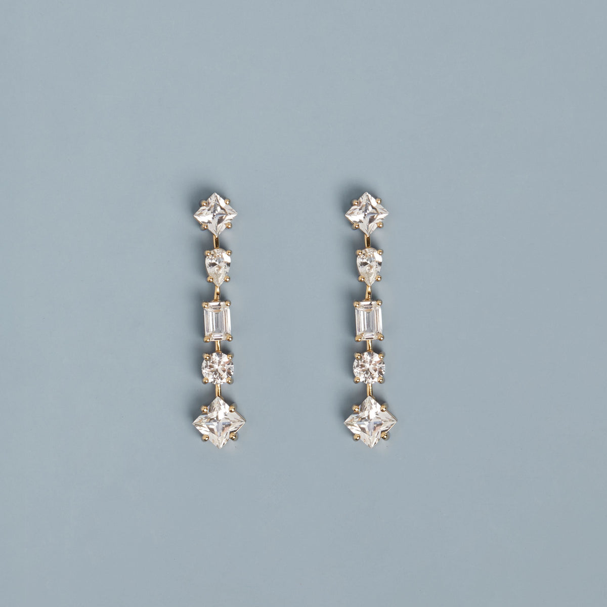 Model. Mixed gemstone tennis earrings on light blue background.