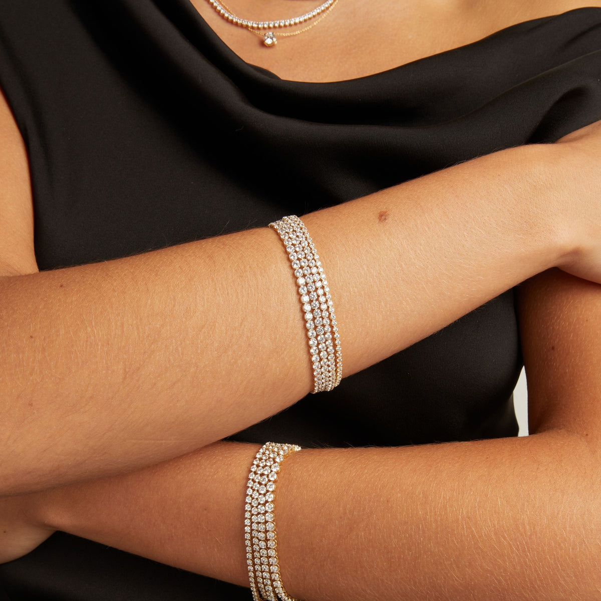 Model. Close up of a woman's crossed arms with stacked diamond tennis bracelets on both wrists.