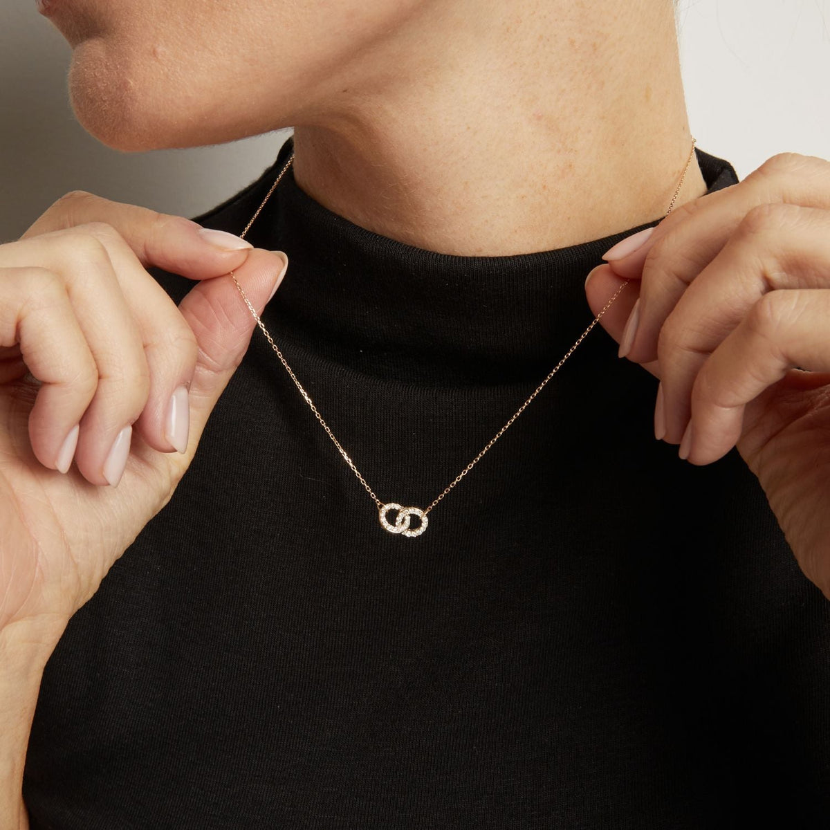 Model. Person wearing a black top with a gold necklace featuring interlocking rings.