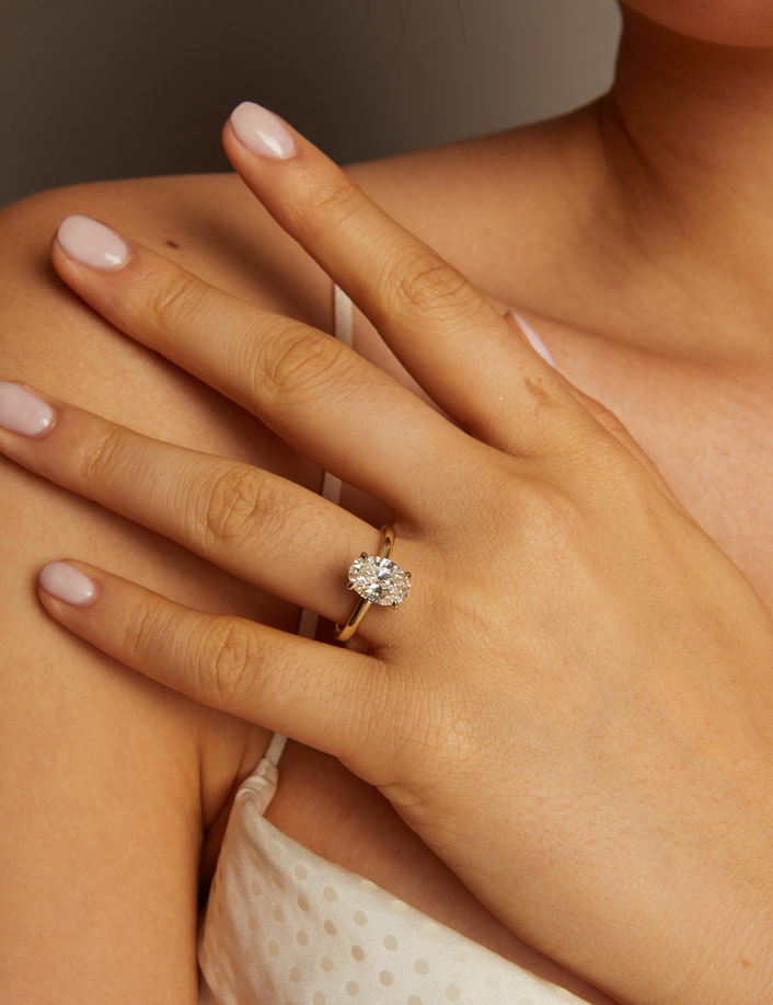 Close-up of a hand wearing a diamond ring on a neutral background