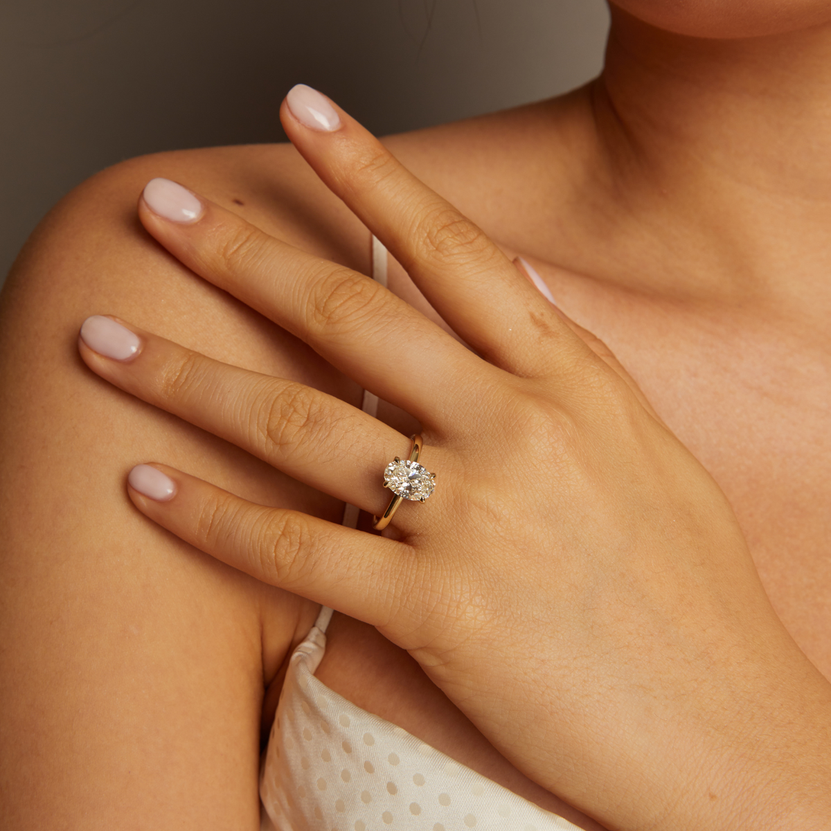 Close-up of a hand wearing a diamond ring on a neutral background