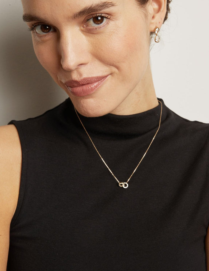 Woman wearing a black sleeveless top and gold necklace with a minimalistic pendant.