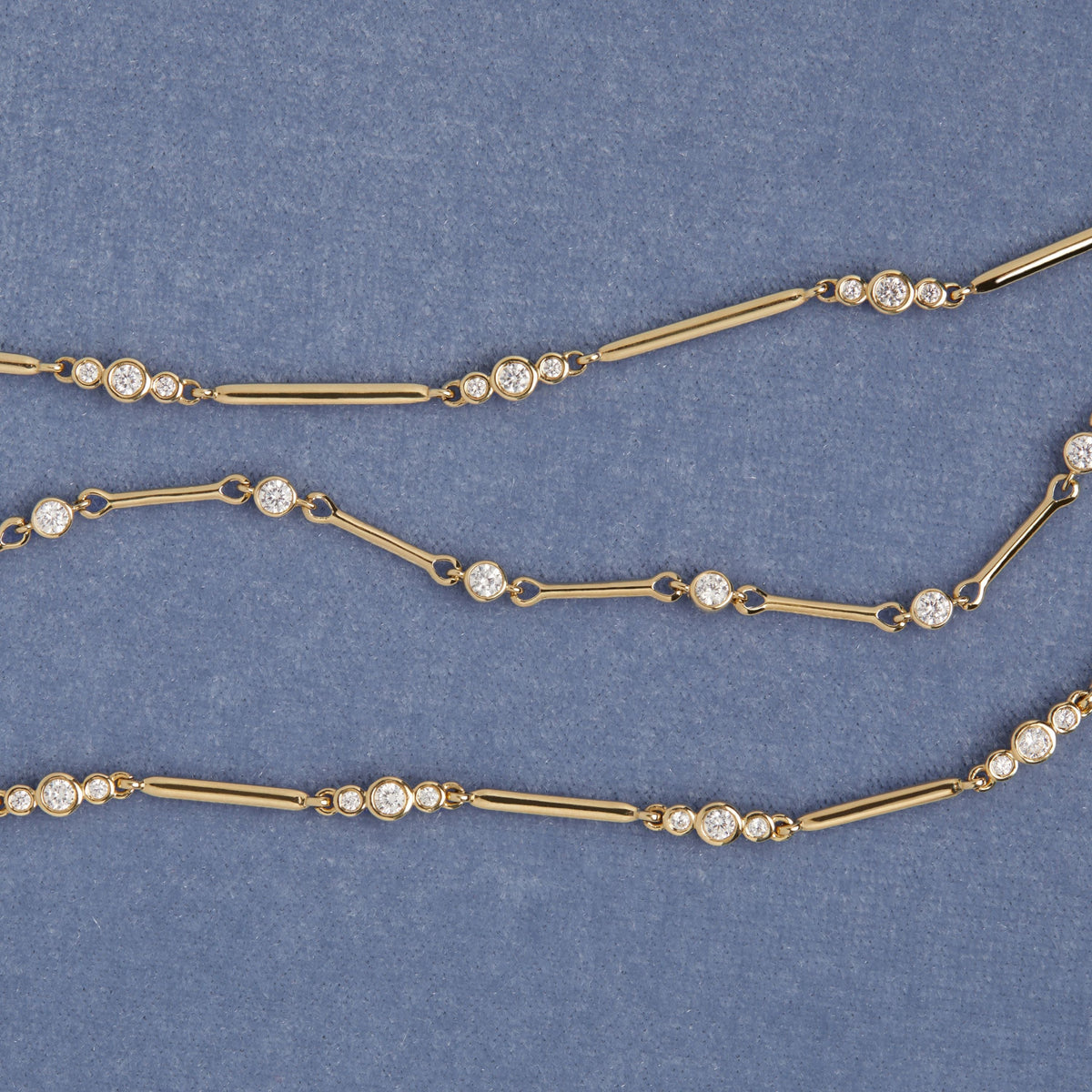 Model. Three gold bracelets with bezel diamonds on blue background