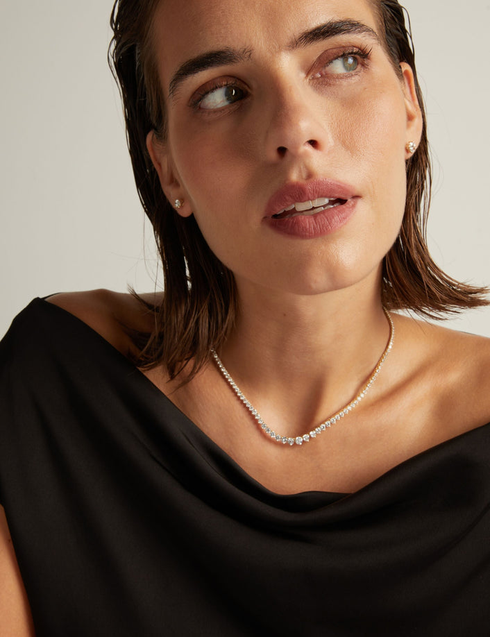 Model. Close up of a woman in a black top wearing a diamond tennis necklace on beige background.
