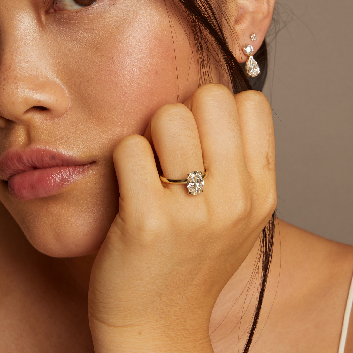 Model. Close-up of a woman wearing a diamond ring and earrings against a neutral background