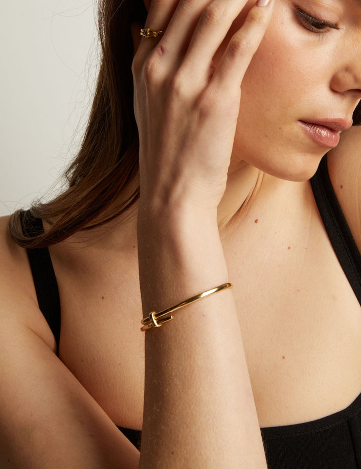 Model. Woman wearing a gold bracelet on her wrist with a neutral background.