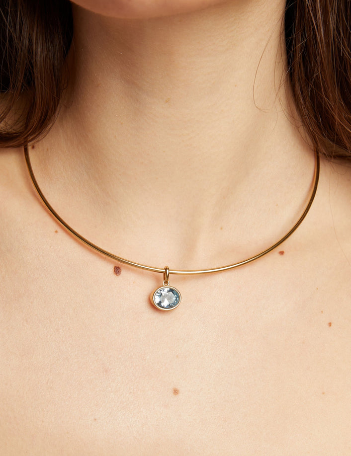 Gold necklace with an aquamarine pendant worn by a woman.