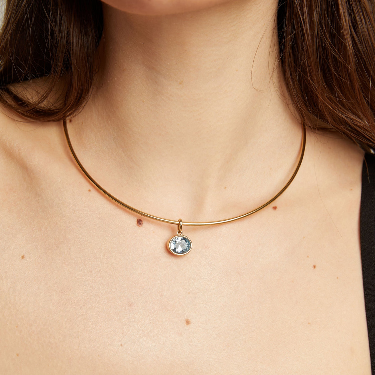 Model. Gold necklace with an aquamarine pendant worn by a woman.