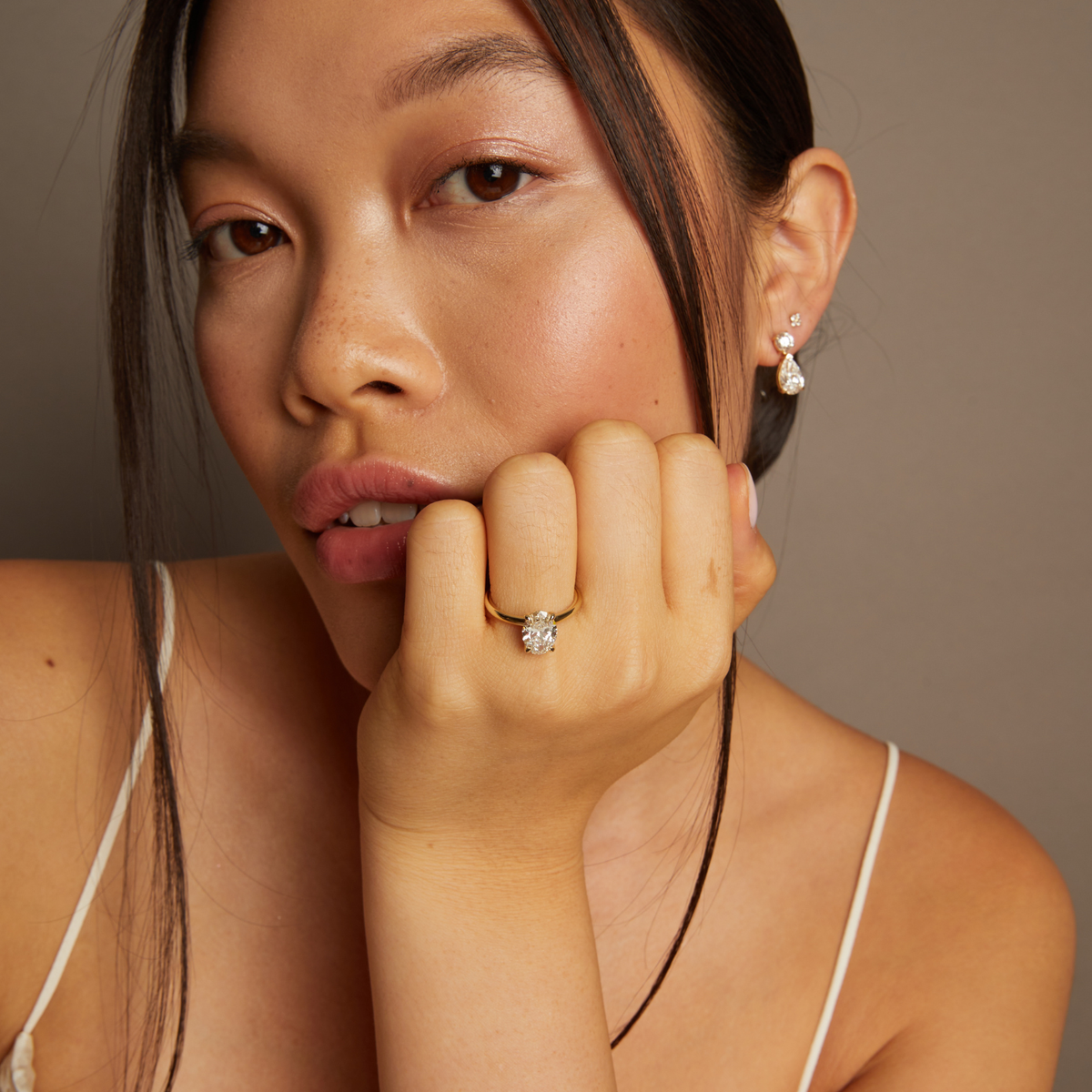 Model. Woman wearing a diamond ring and earrings against a neutral background