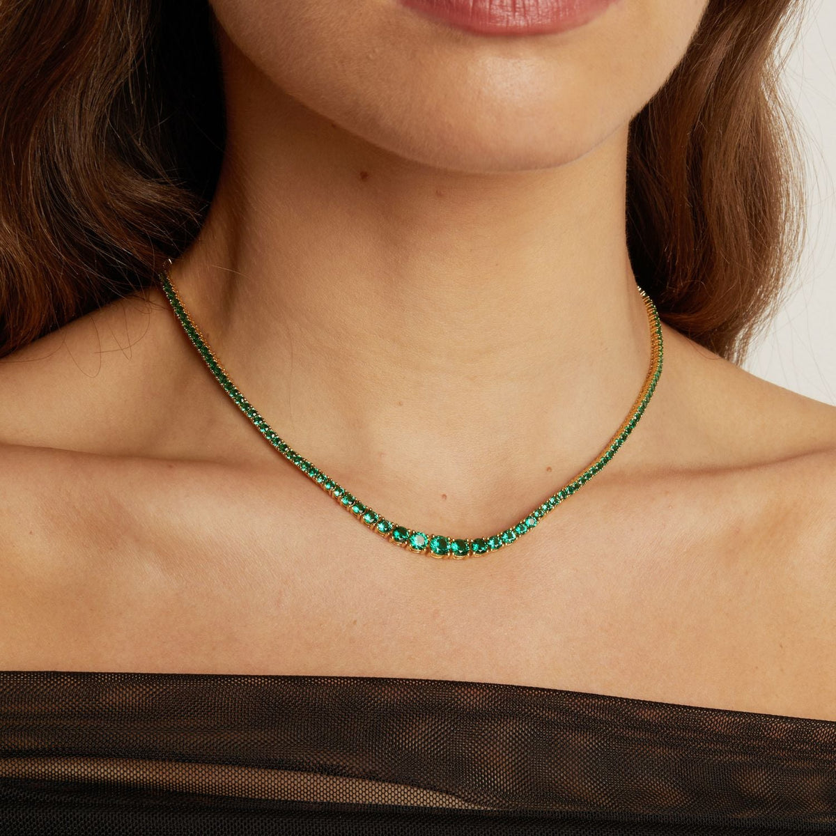 Model. Close-up of a person wearing a green gemstone necklace against a neutral background