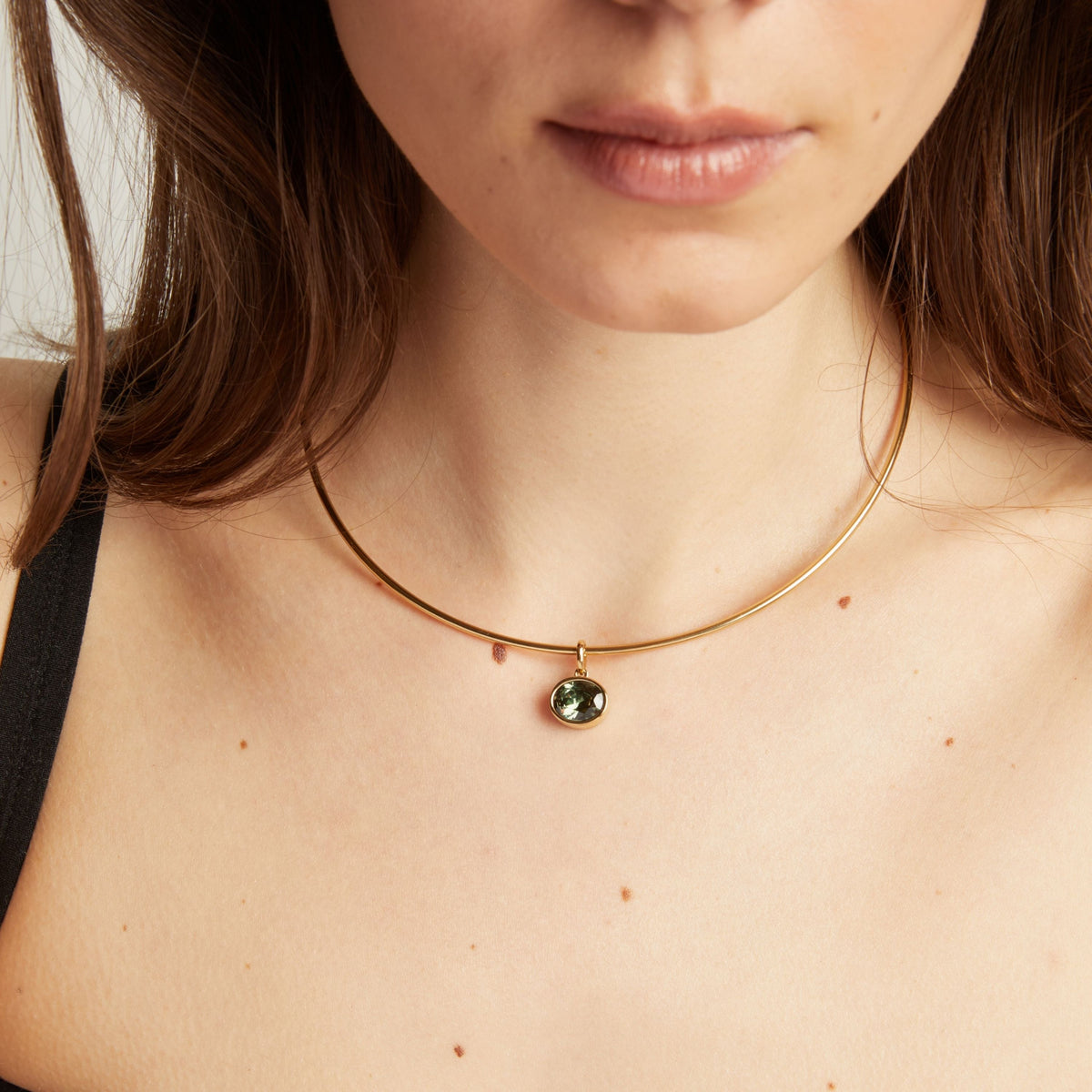 Model. Close up of a woman wearing a gold necklace with a green gemstone pendant.