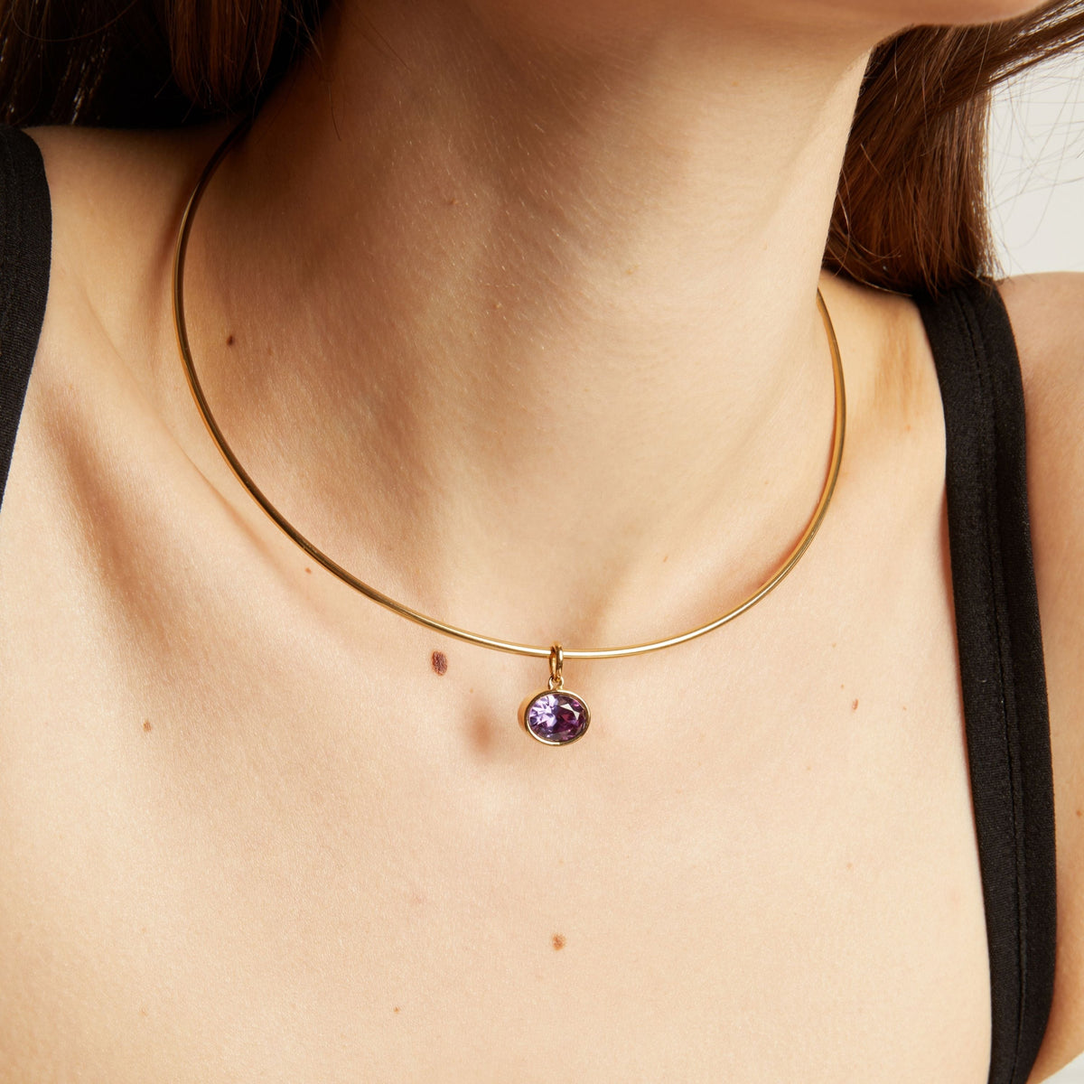 Model. Close up of a woman wearing a gold necklace with an amethyst pendant.