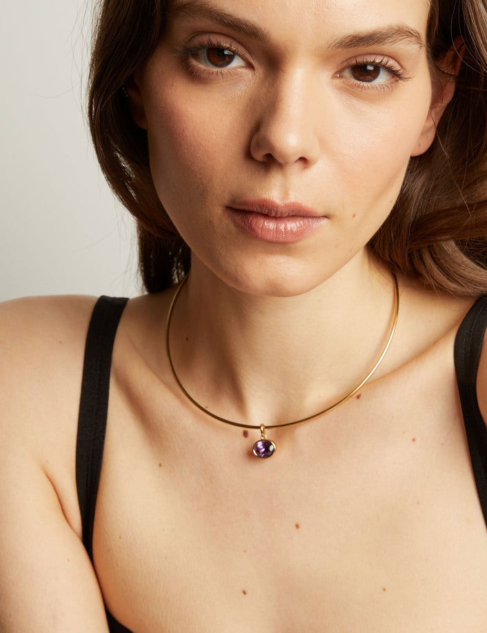Woman wearing a gold necklace with an amethyst pendant.