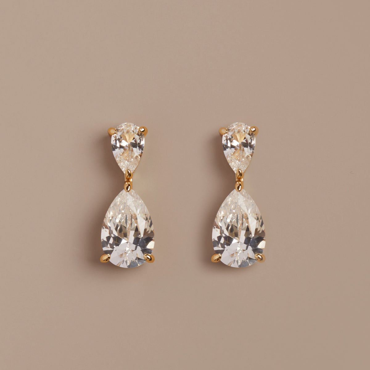 Model. Pair of teardrop-shaped crystal earrings on a beige background