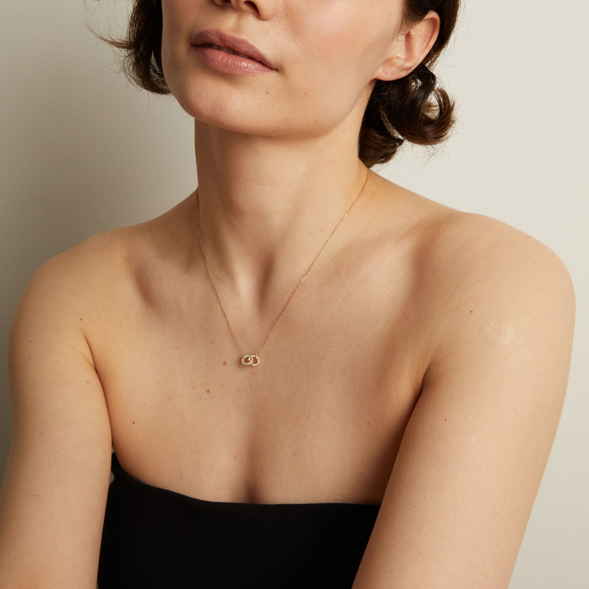 Model. Woman wearing a delicate gold necklace against a neutral background