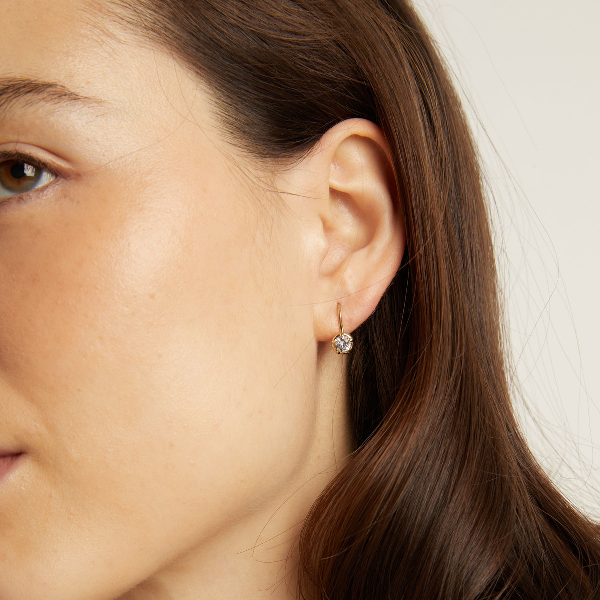 Model. Close-up of a woman's ear wearing a diamond earring with a blurred background