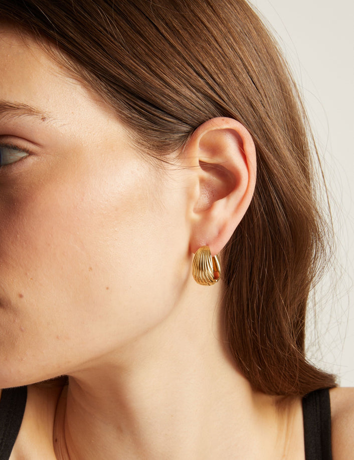 Model. Close up of a woman wearing gold hoop earrings with a neutral background.