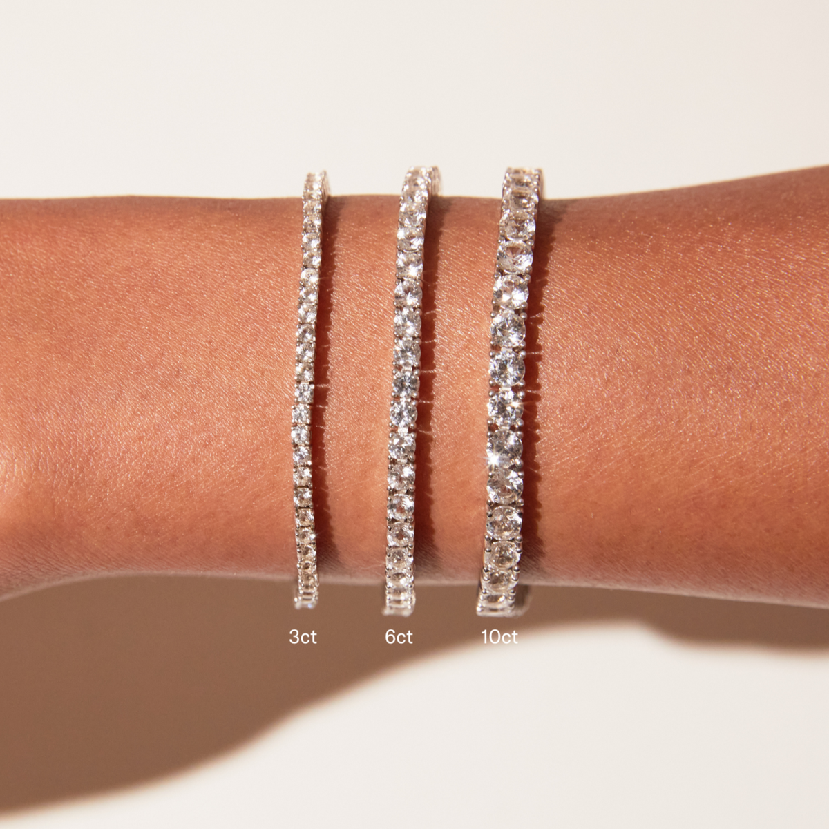 Model Close-up of a woman wearing three stacked white sapphire tennis bracelets, with text overlays labeling them '3ct', '6ct', and '10ct
