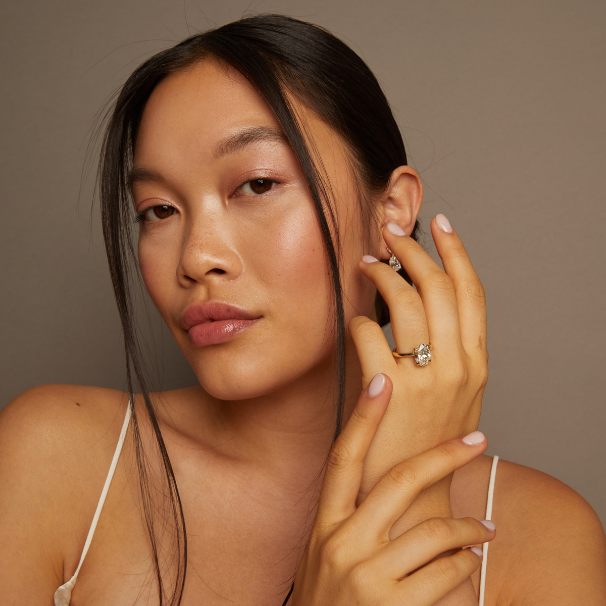 Model. Woman wearing a diamond earring and ring against a neutral background