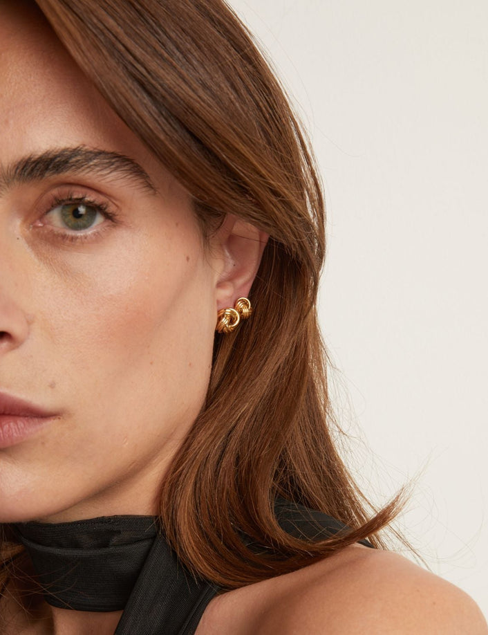 Model. Close-up of a woman wearing gold earrings with a neutral background