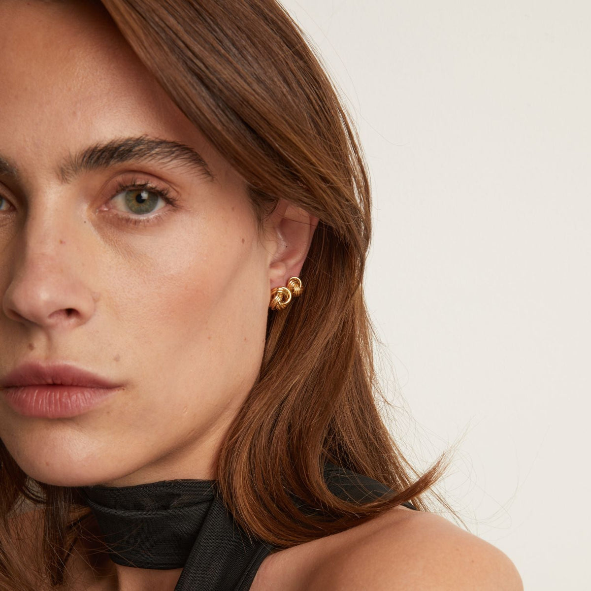 Model. Close-up of a woman wearing gold earrings with a neutral background