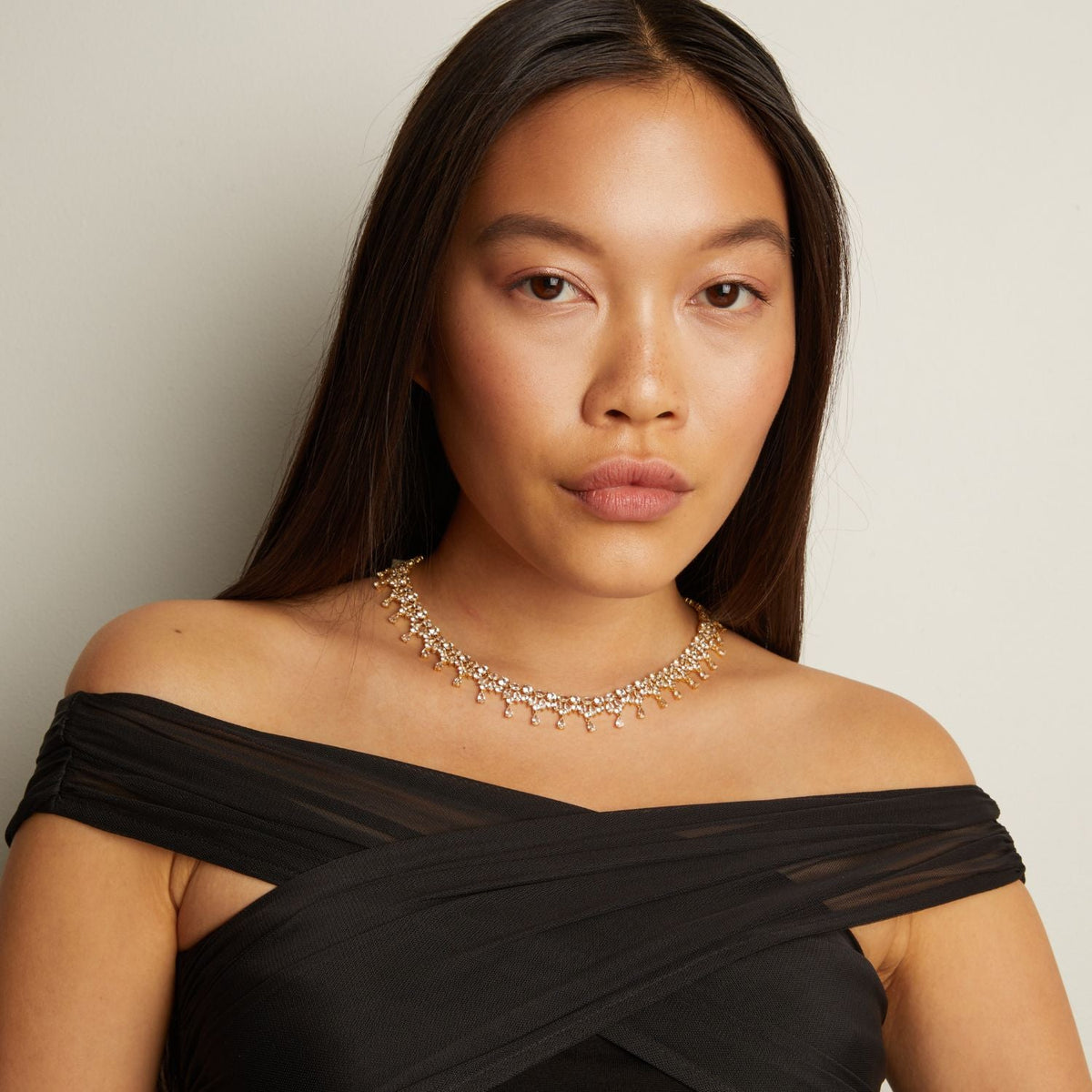 Woman wearing a black off-shoulder top and a decorative necklace against a neutral background