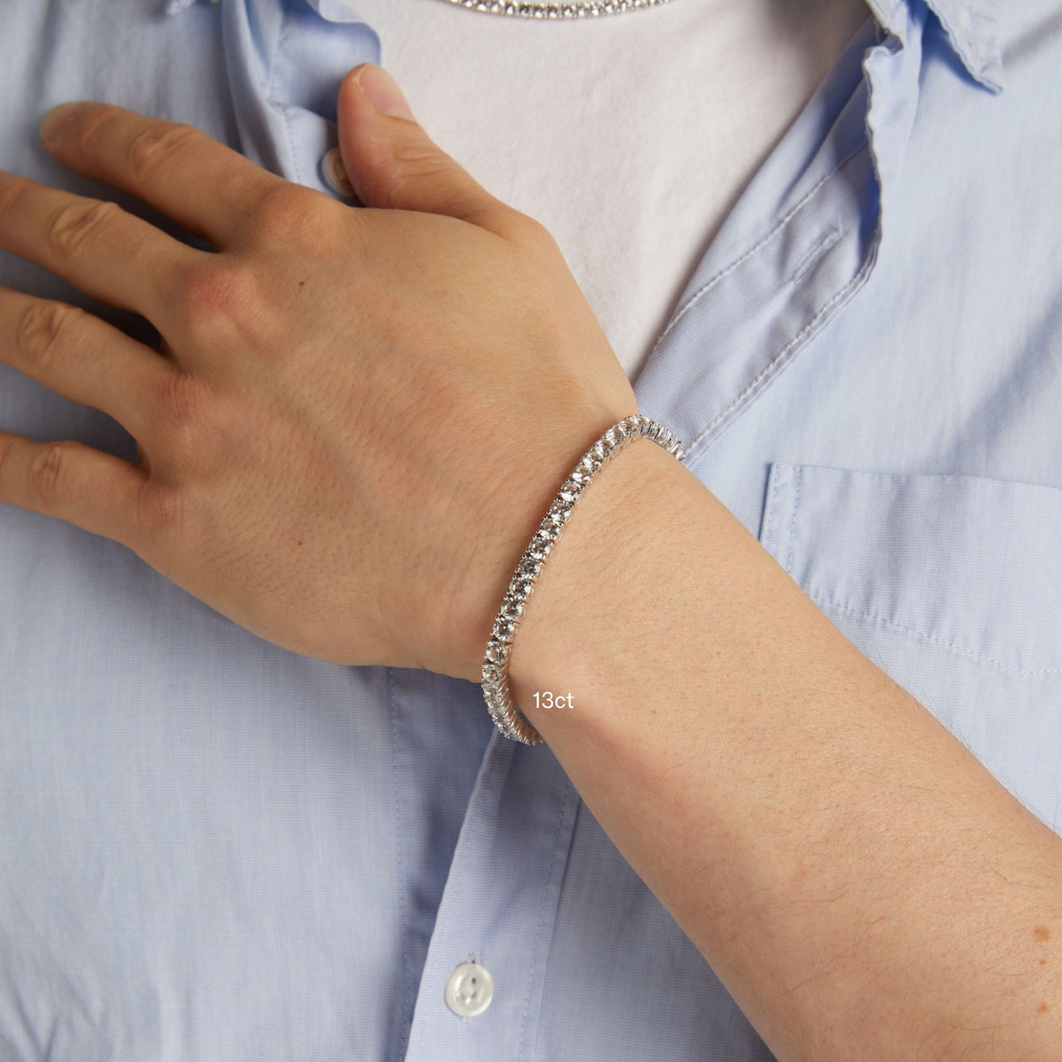 Model. A close-up of a man's wrist wearing a delicate tennis bracelet, shown against a light blue button-down shirt.