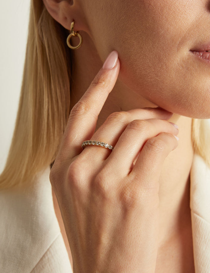 Model. Close-up of a woman wearing gold earrings and a ring, with a neutral background.
