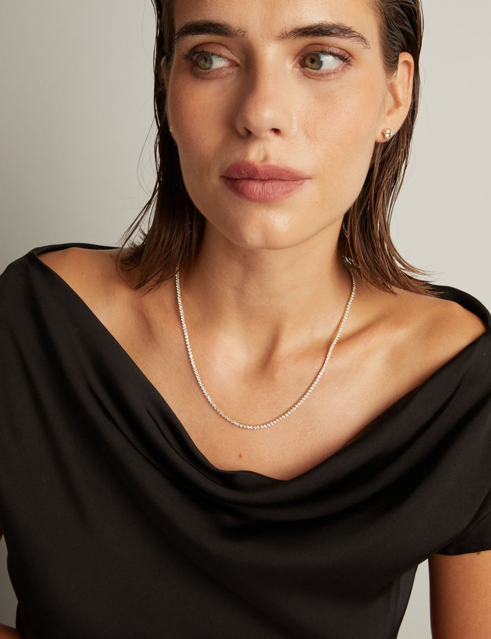 Model. Close up of a woman in a black top wearing a diamond tennis necklace on beige background.