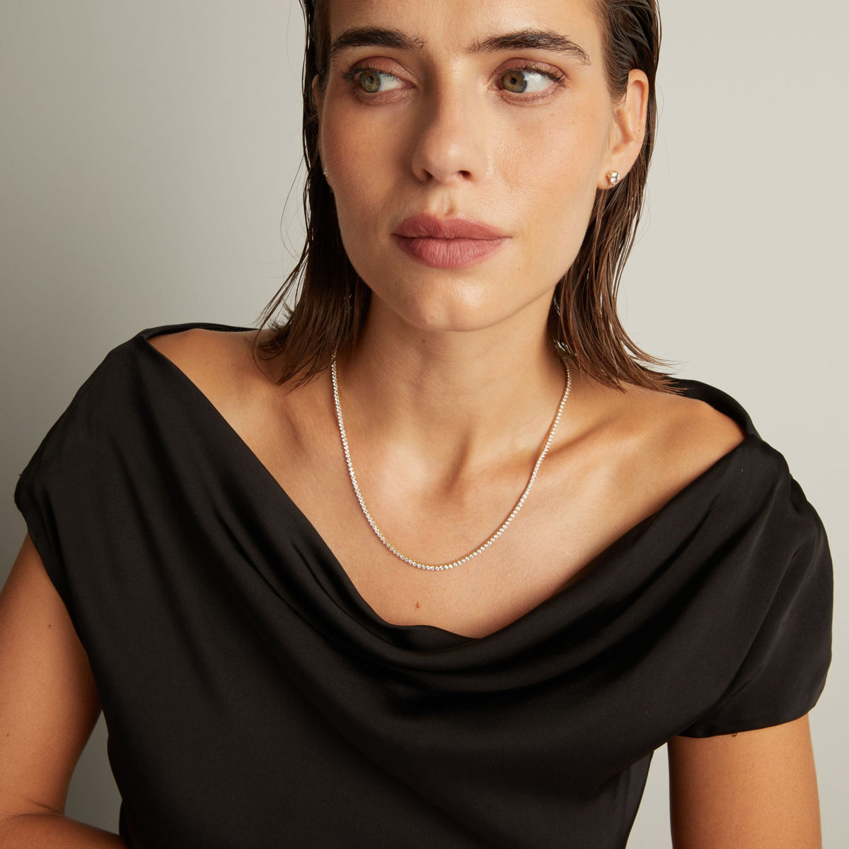 Model. Close up of a woman in a black top wearing a diamond tennis necklace on beige background.